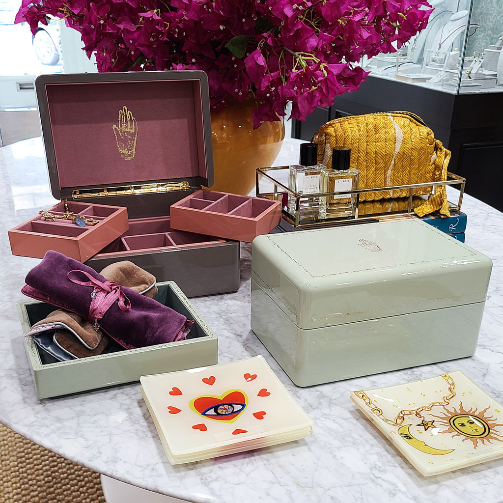 Jewelry boxes and other gift items laying on a marble table in front of a bouquet of pink flowers